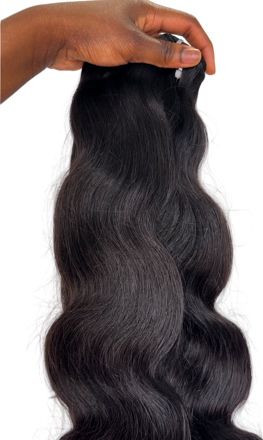 Black hair extensions held by a hand on a white background